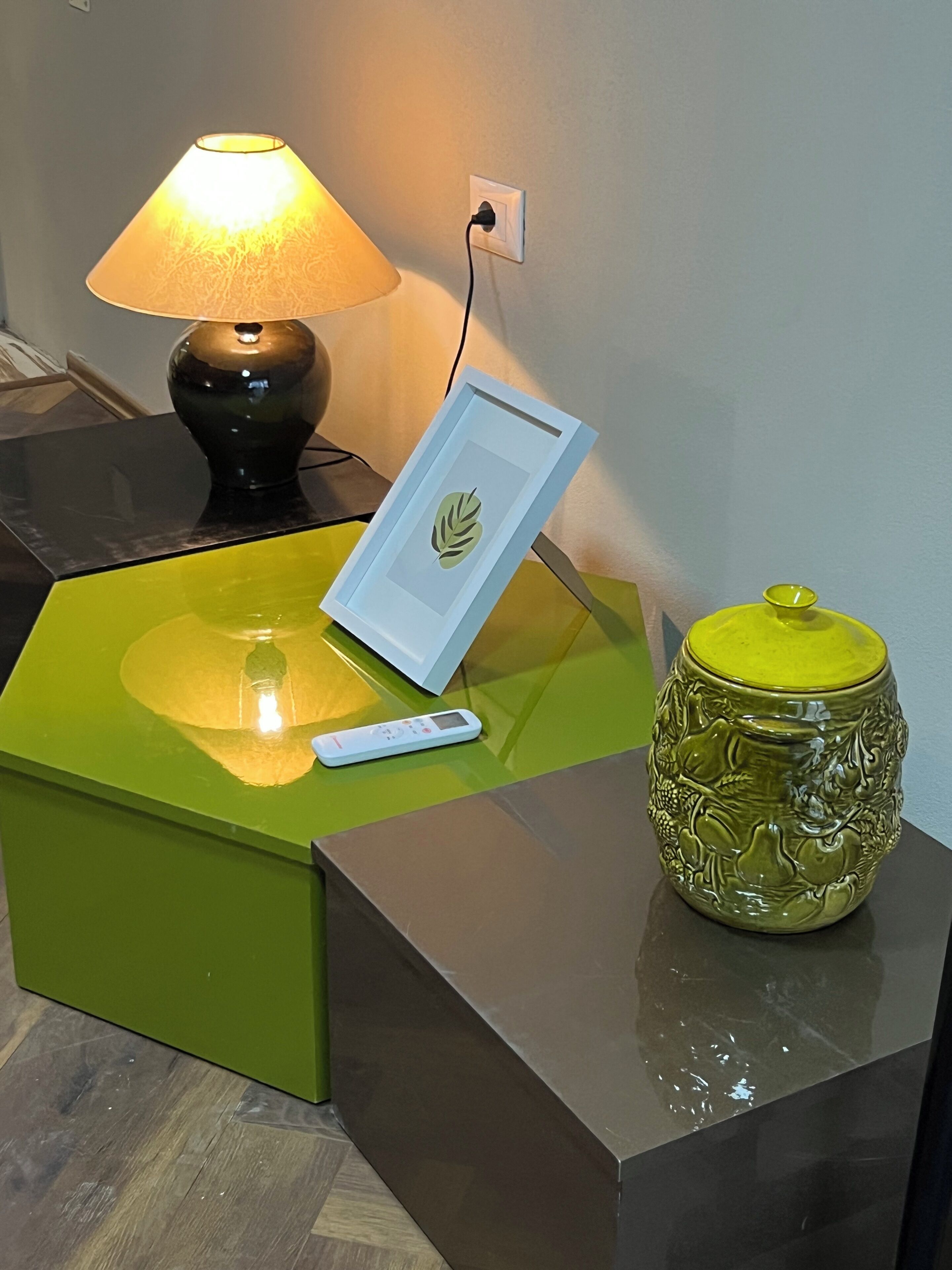 Ett sidobord med en lampa, en inramad bild, en fjärrkontroll och en dekorativ vas.