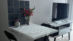 A dining area with a table, chairs, a vase with flowers, a flat-screen TV, and a herringbone-patterned floor.