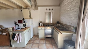 Une cuisine compacte équipée d’une cuisinière, d’un évier et d’un four à micro-ondes. On y trouve un petit plan de travail et un meuble avec une étagère suspendue.