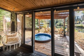 A wooden deck with a hanging chair, a hot tub, and outdoor furniture. - Hills Haven - Luxury Riverfront Cottage (Minden Hills)