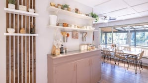 A kitchen with wooden shelves, a dining area with wicker chairs, and a large window. - Hills Haven - Luxury Riverfront Cottage (Minden Hills)