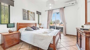 Ein Schlafzimmer mit Bett, Nachttisch, Lampe, Kunstwerk und Blick ins Freie.