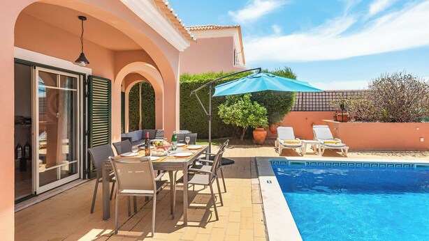 Ein Poolbereich mit Esstisch, Stühlen und einem blauen Sonnenschirm.