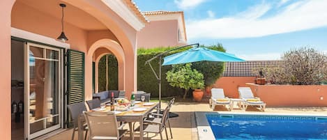 A poolside area with a dining table, chairs, and a blue umbrella.