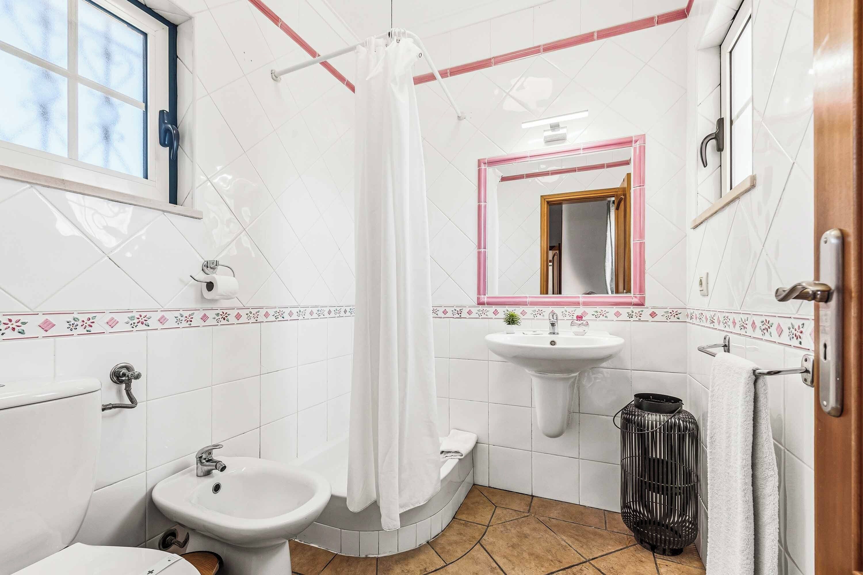 A bathroom with a toilet, bidet, sink, shower curtain, mirror, and a towel rack.