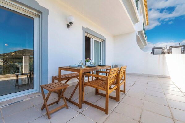 A balcony with a wooden table and chairs, a glass door, and a view of the landscape. -  Loule Hill - Lua Villa (Faro)