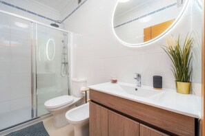 A modern bathroom with a glass-enclosed shower, a toilet, a sink with a mirror, and a potted plant. -  Loule Hill - Lua Villa (Faro)