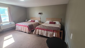 A hotel room with two beds, a desk, a chair, a lamp, and a window with curtains. - Vanscoy Motel (Vanscoy)