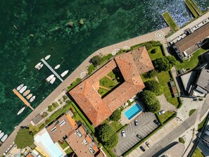 An aerial view of a coastal property with a swimming pool, boats docked nearby, and a mix of residential and commercial buildings. - Appartamento Valentina (Paratico)