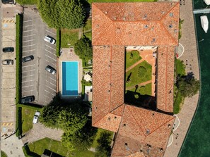 An aerial view of a building with a swimming pool, parking area, and a waterfront. - Appartamento Valentina (Paratico)
