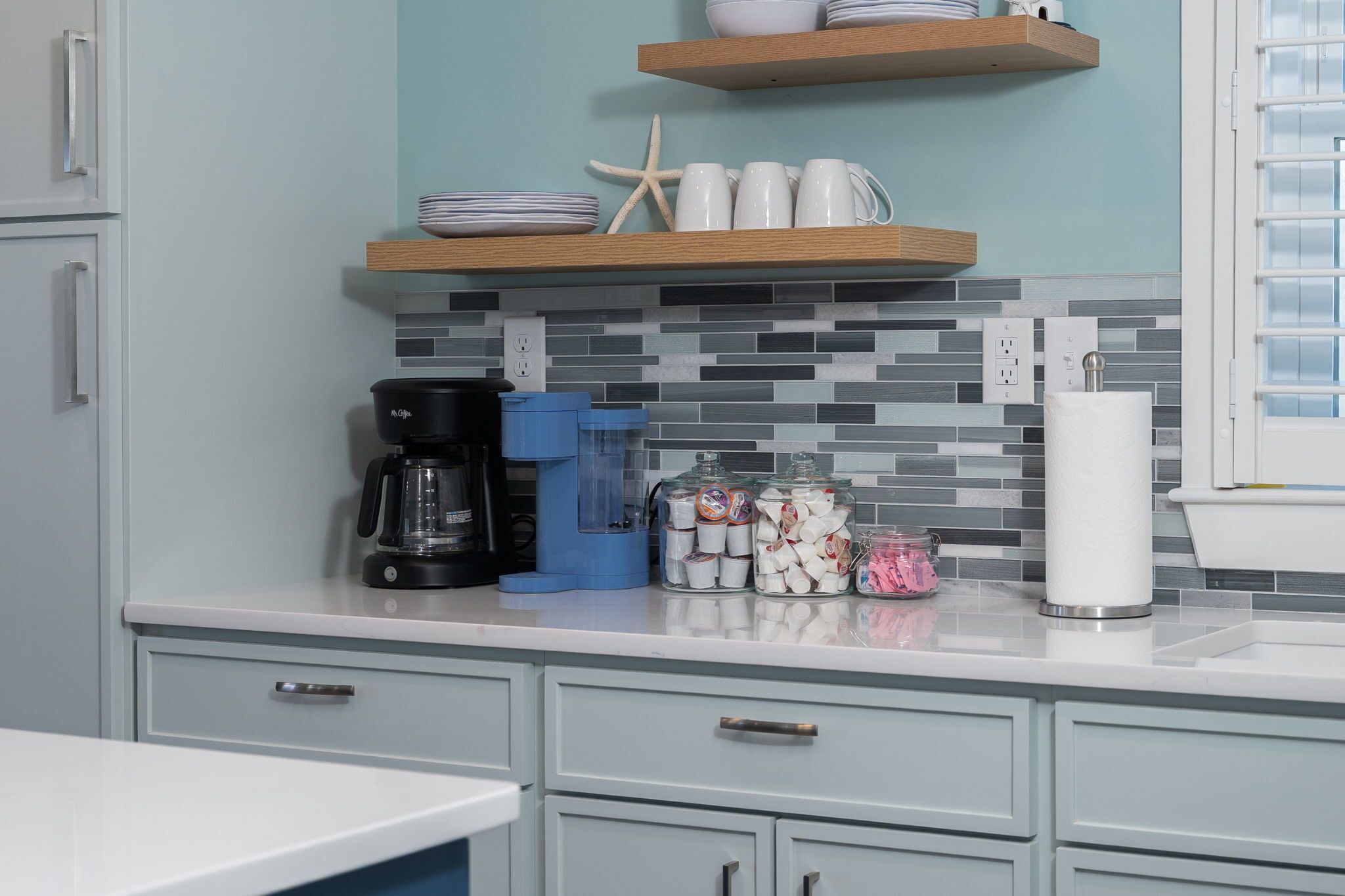 A kitchen with a coffee maker, a blender, jars of snacks, and a roll of paper towels.