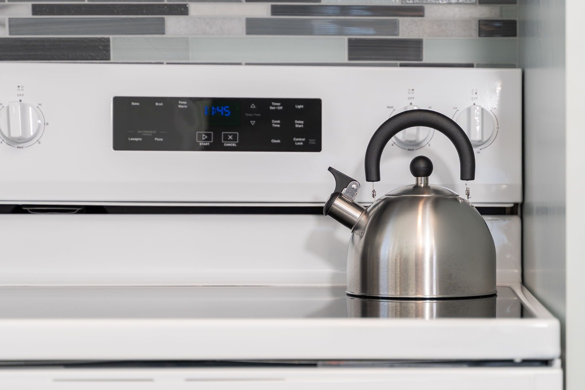 A stainless steel kettle on a white oven with a digital control panel displaying the time as 1:45.