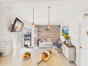 Eine moderne Küche mit Essbereich, ausgestattet mit einer zentralen Kochinsel mit Obst und Käse, Pendelleuchten und Blick ins Freie.