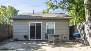 A residential backyard with a sliding glass door, a patio table with chairs, a barbecue grill, and a wooden fence.