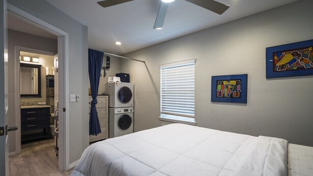 A bedroom with a bed, a ceiling fan, a washing machine, and a window with blinds. - Charming Casita | Couple Haven | Walk to OU Campus (Norman)