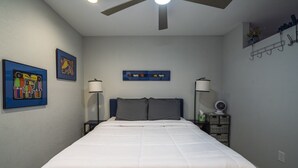 A bedroom with a bed, two wall-mounted lamps, a ceiling fan, and framed artwork on the walls.