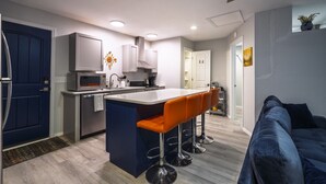 A modern kitchen with a central island, bar stools, and a blue door. - Charming Casita | Couple Haven | Walk to OU Campus (Norman)