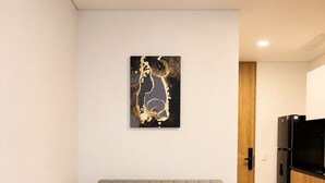 A modern living room with a grey sofa, a wooden floor, a kitchen area, and a wall-mounted abstract art piece. - Apartment with incredible city view (Bogotá)