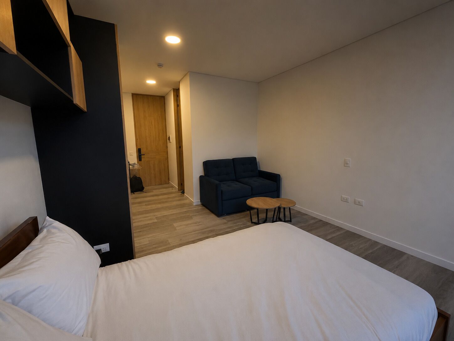 Ett hotellrum med en säng, ett litet runt bord, en soffa och en dörr av trä.