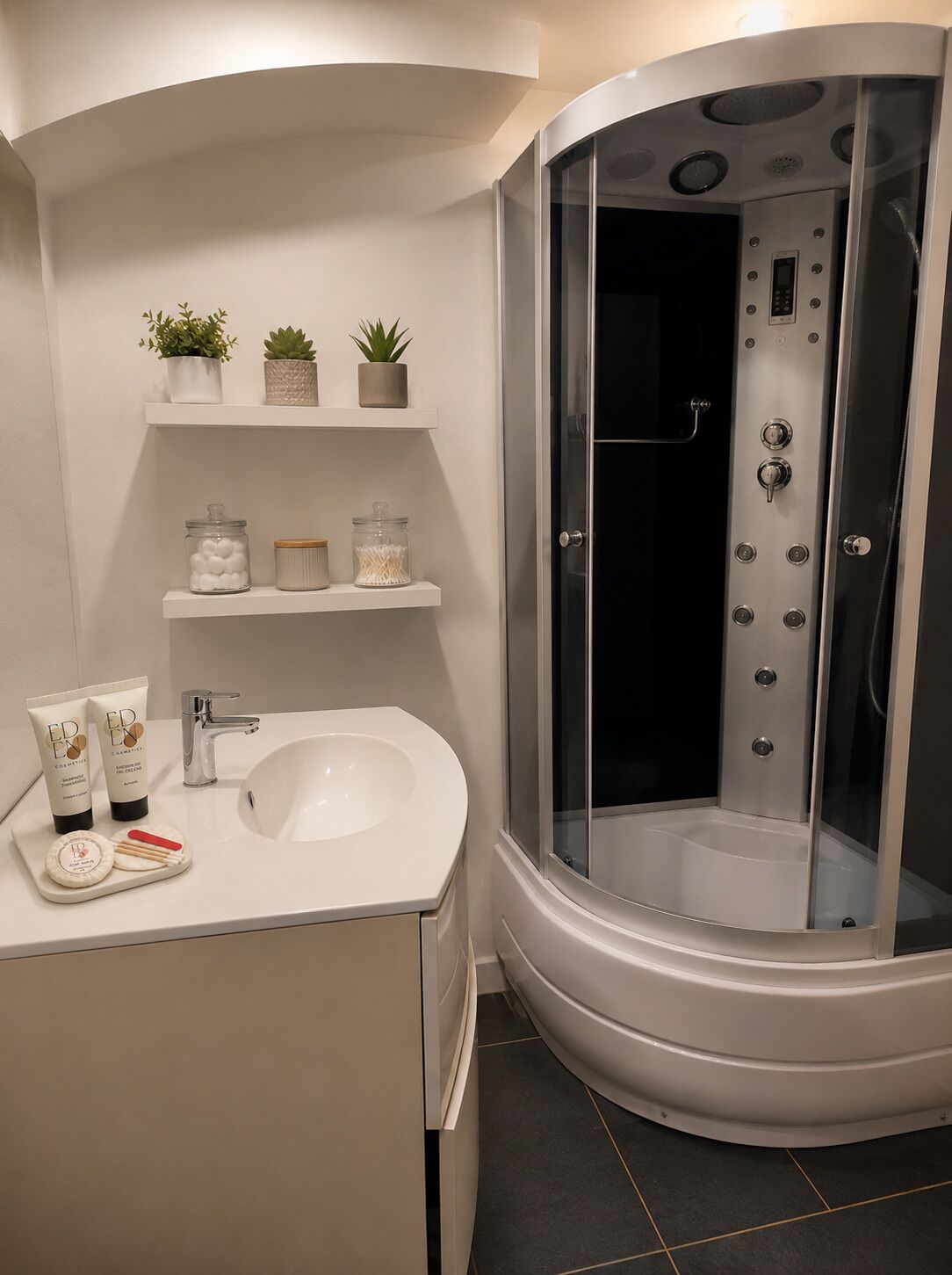 A modern bathroom with a curved shower enclosure, a white sink, and a vanity with toiletries.