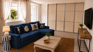 A living room with a blue sofa, a small table, a TV, and a sliding door. - The Nathéa Suite, 10 minutes from Sainte-Maxime (Roquebrune-sur-Argens)