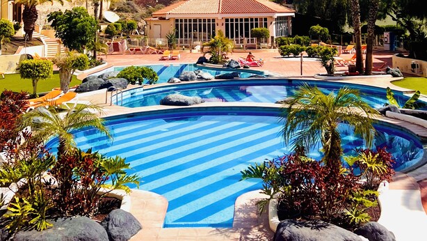 Un resort con una grande piscina, palme e un edificio dal tetto rosso.