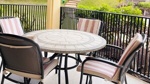 Una veranda coperta con un tavolo rotondo e sedie, un soffitto giallo e vista su un giardino curato con alberi e una recinzione.