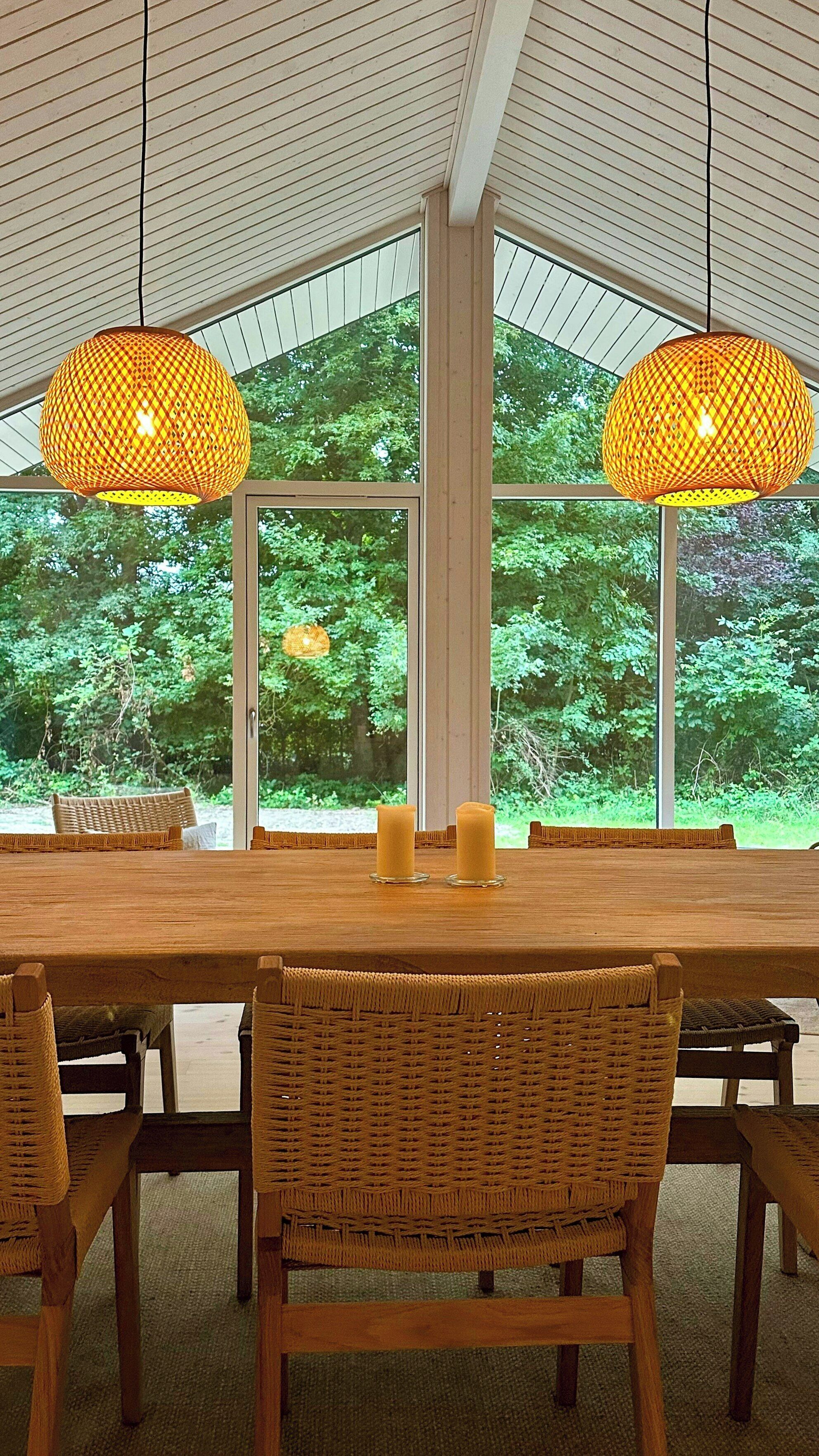 Un coin repas avec une table en bois, des chaises en osier et deux lampes suspendues.