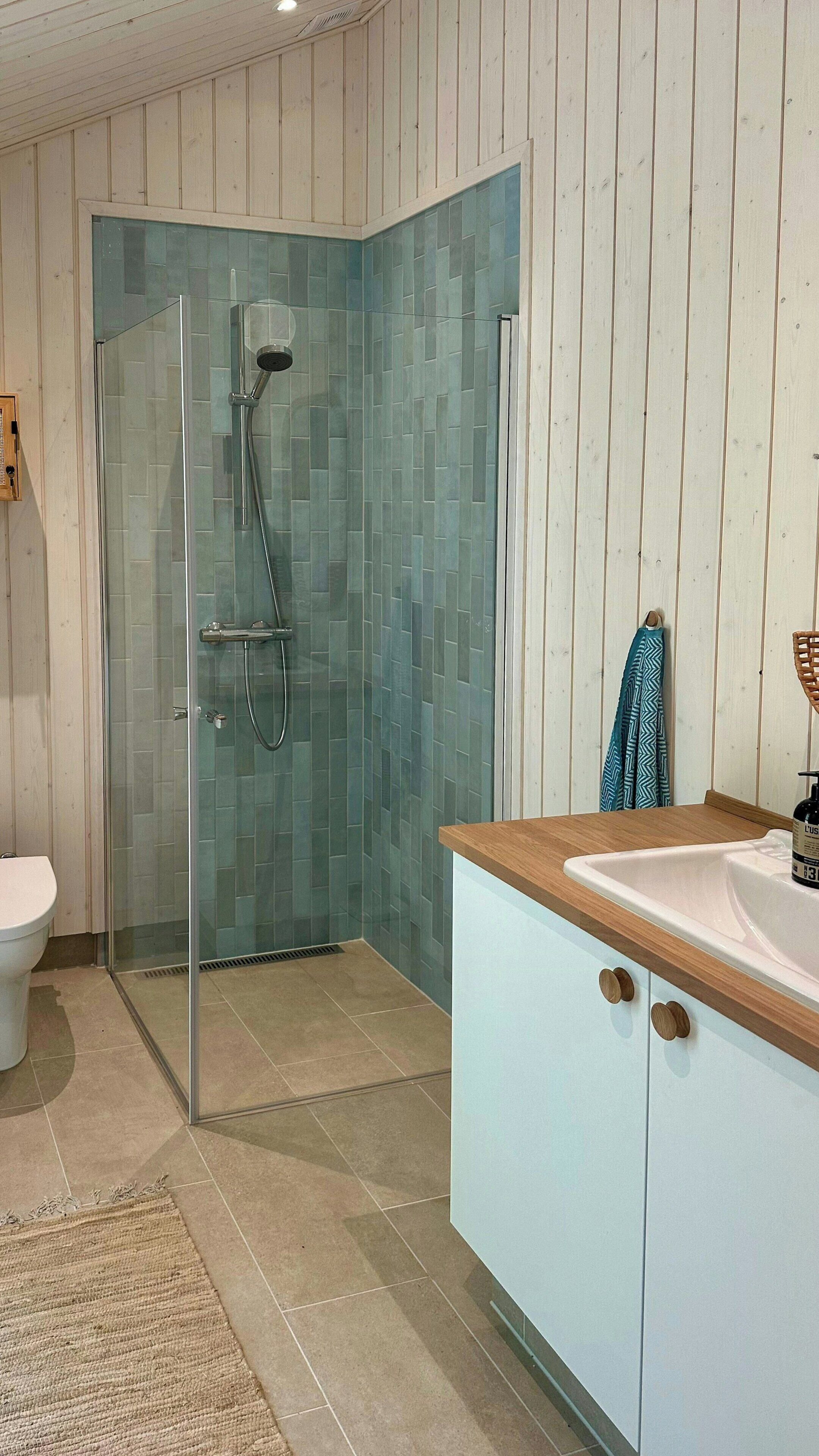A bathroom with a glass shower enclosure, a white sink, and wooden cabinetry.