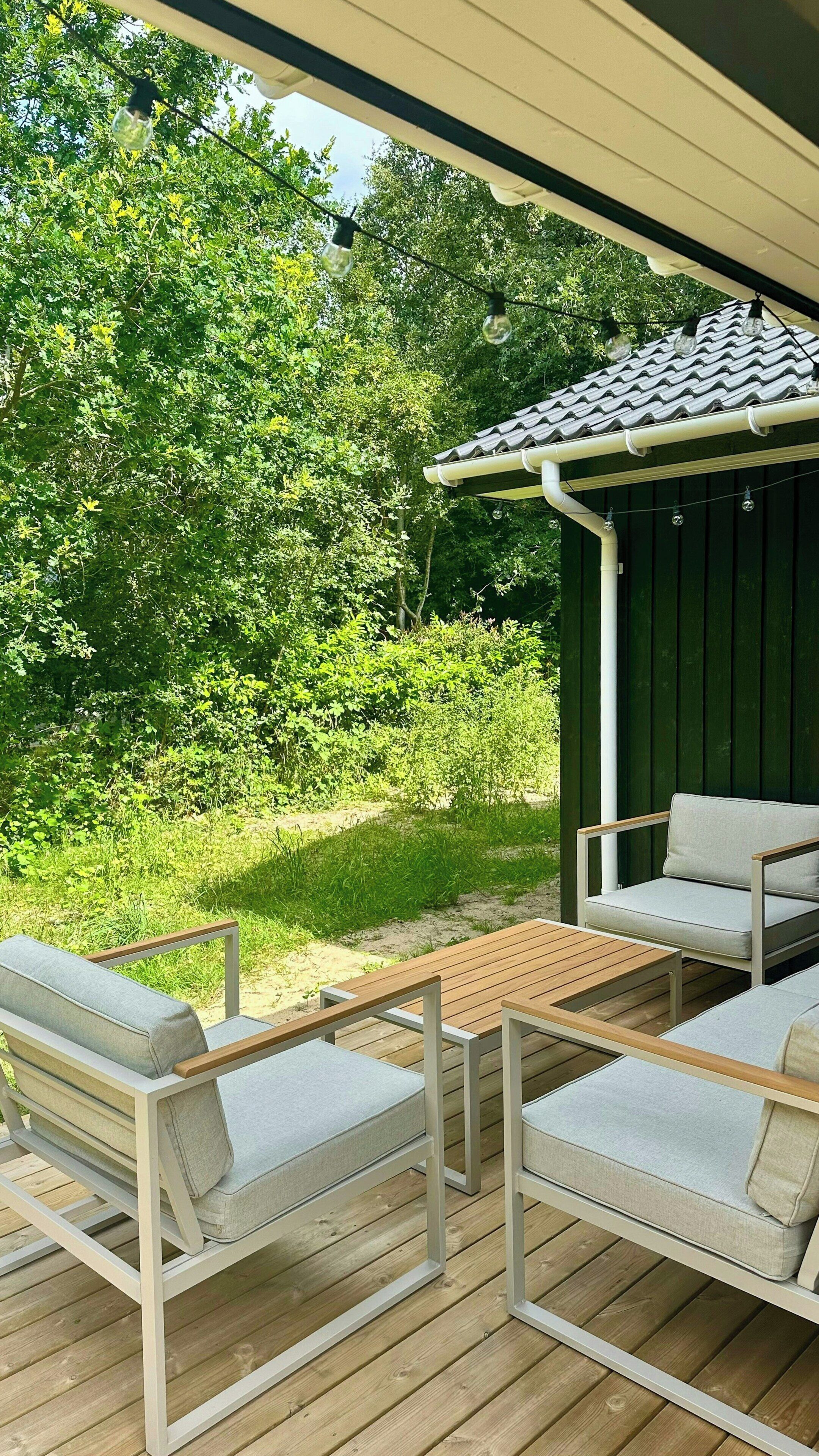 Ein Sitzbereich im Freien mit Holzterrasse, weißen Polsterstühlen und einer Pergola mit Ziegeldach.