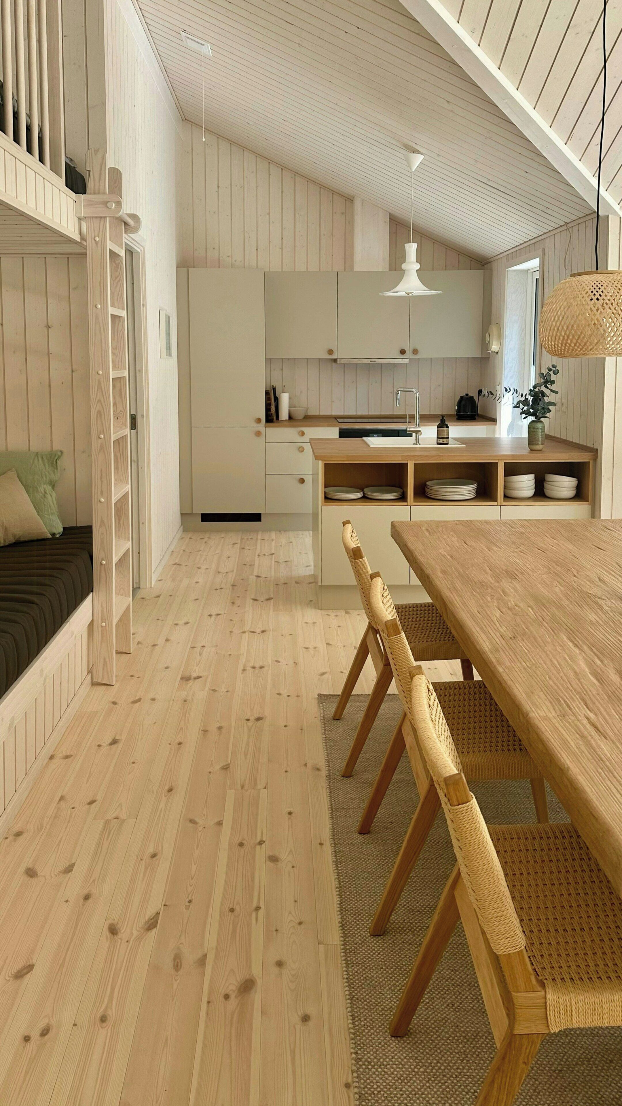 A modern kitchen with wooden cabinets, a dining area with a wooden table and chairs, and a loft bed with a ladder.