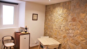 Une pièce de taille modeste avec un mur en pierre, une petite table en bois, une chaise, un réfrigérateur compact et une fenêtre.