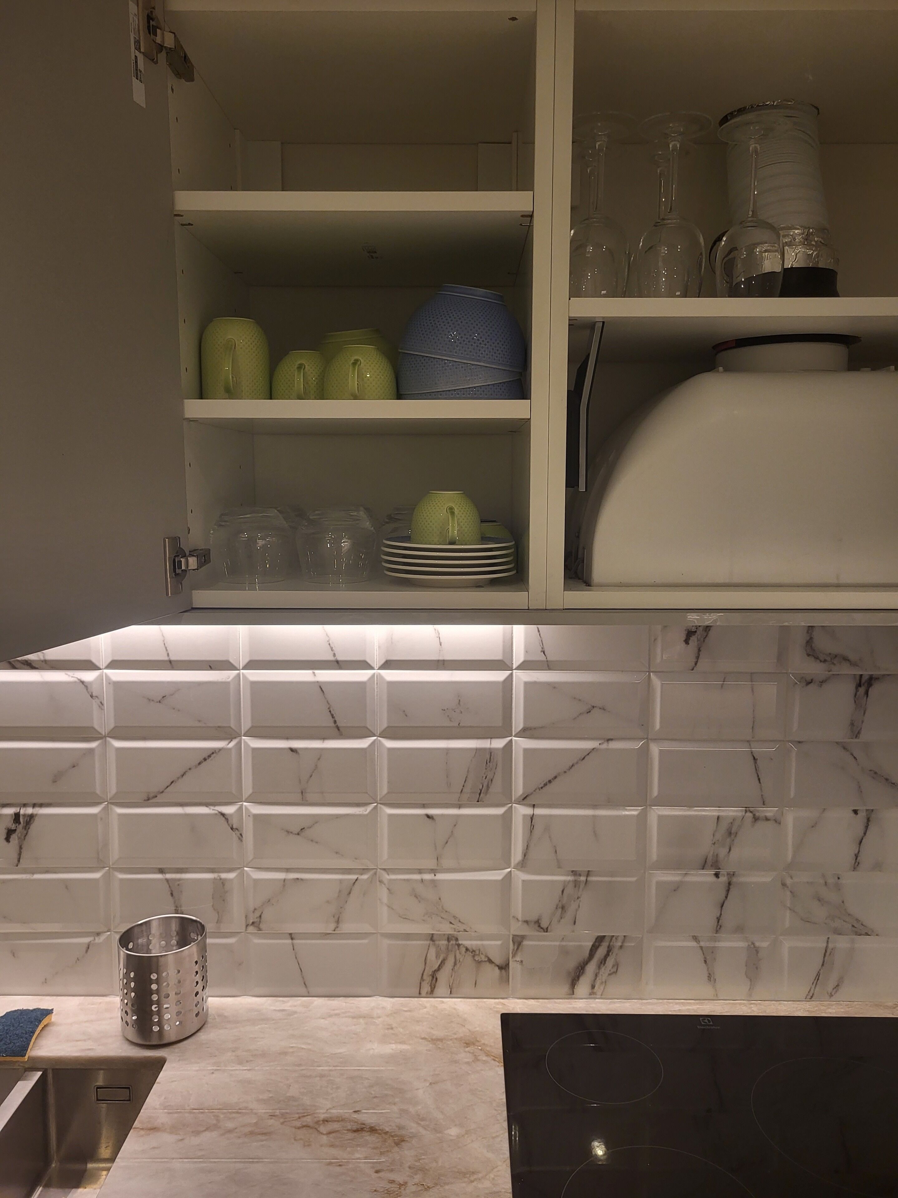 Una cocina con protector contra salpicaduras de mármol, un lavamanos y un mueble con vajilla y vasos.