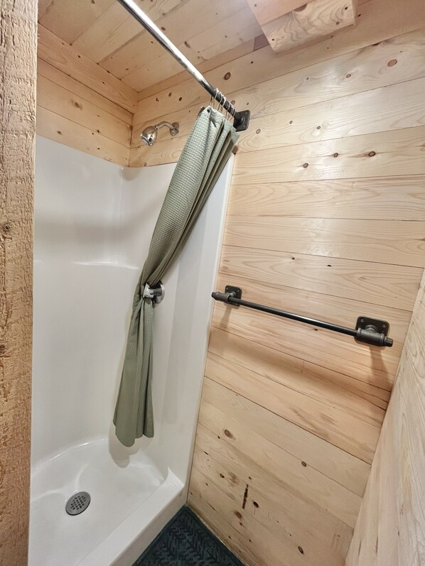 Ein Badezimmer mit Holzwandverkleidung, einer Dusche, einem Handtuchhalter und einer Metall-Handläufe.