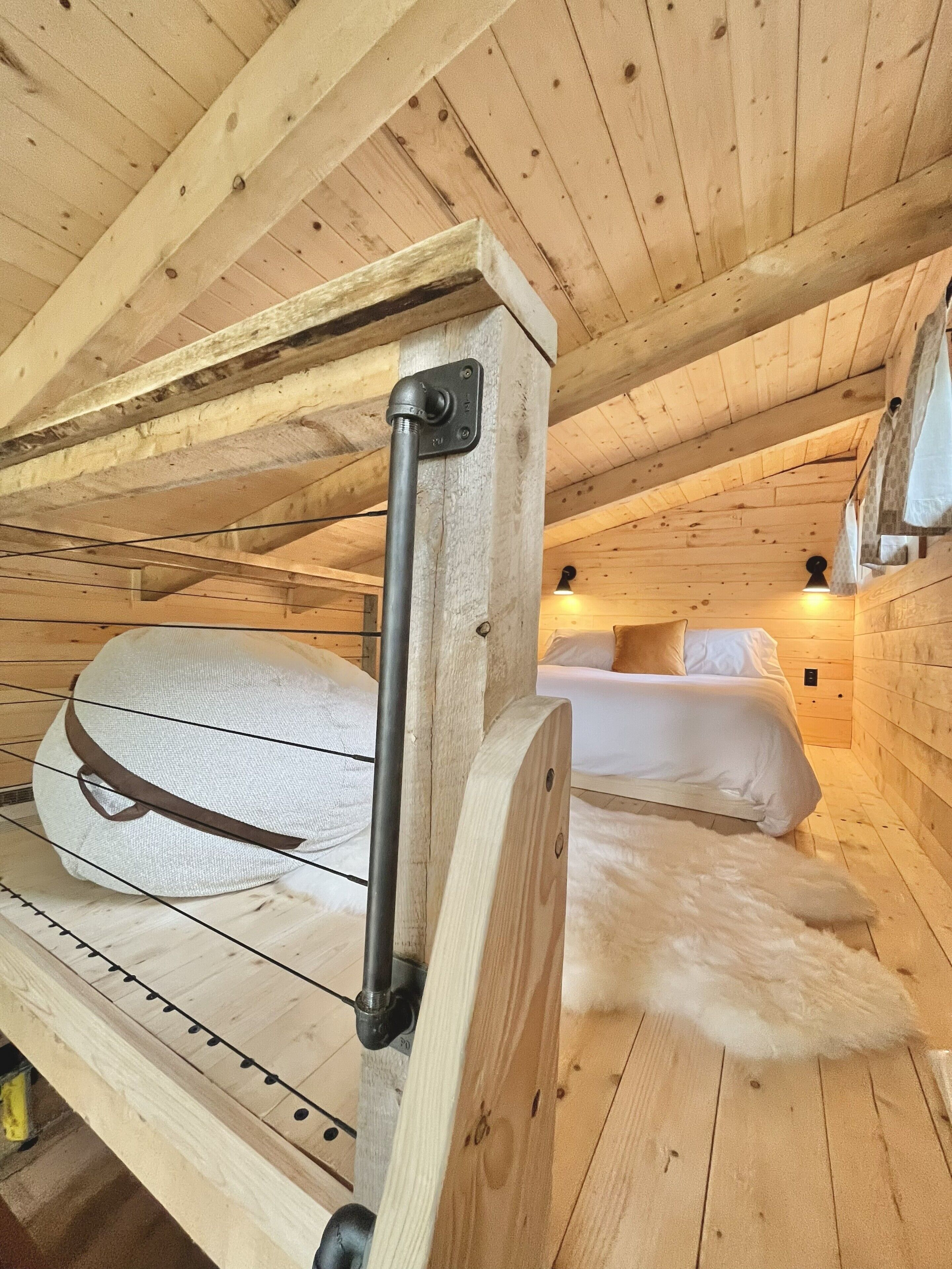 A wooden cabin interior with a bunk bed, a metal support beam, and a bed with white bedding.