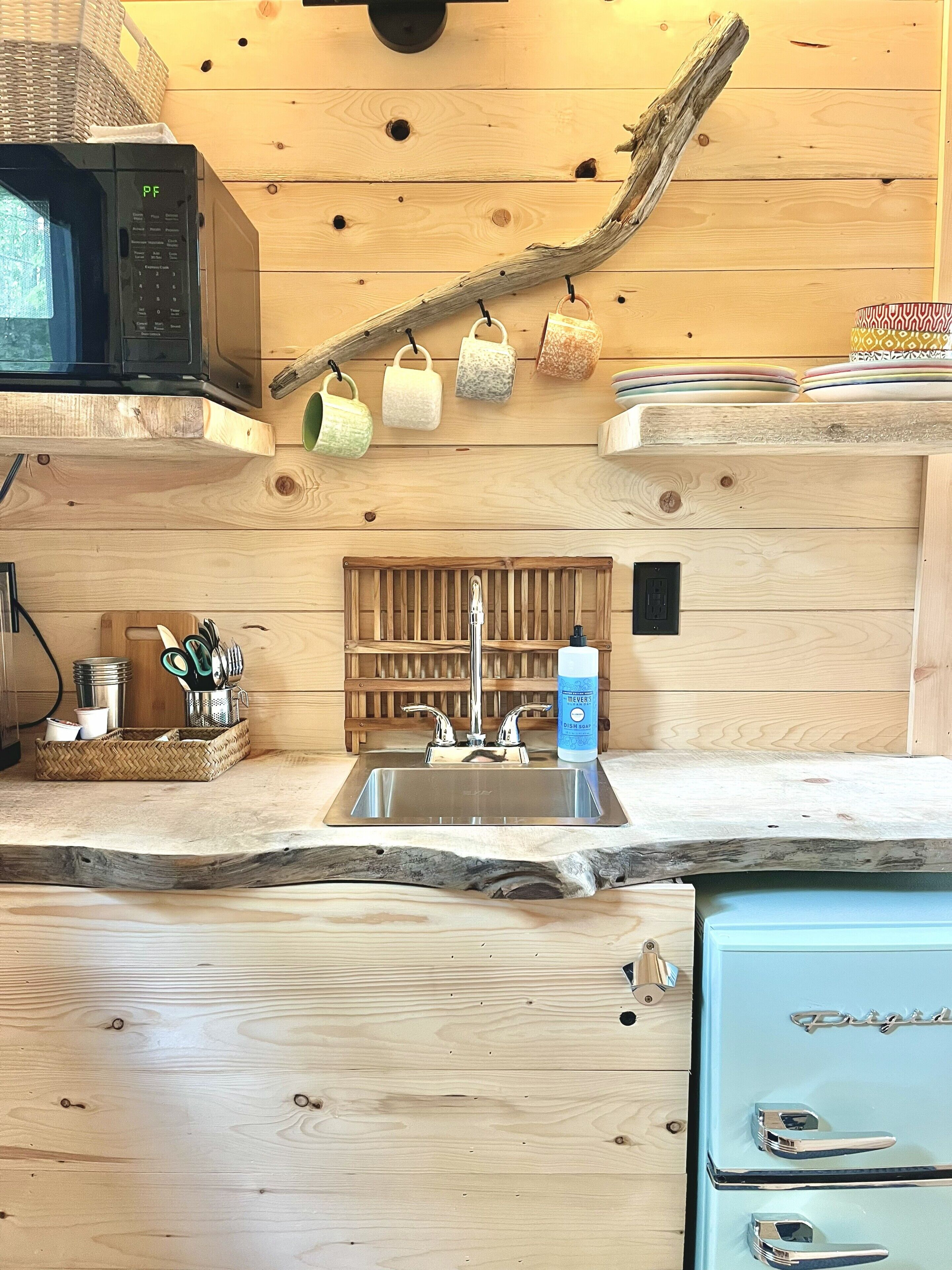 A kitchen with a wooden theme, featuring a microwave, a sink, and a dish soap bottle.