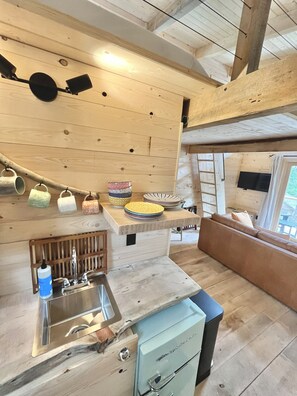 Une cuisine de taille réduite, équipée d’un évier, d’un petit réfrigérateur et d’un plafond en bois.