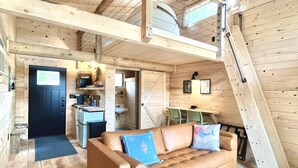 Amplio espacio tipo loft con techo alto, ventilador de techo, sofá con cojines decorativos, zona de comedor con mesa y sillas, y espacio de cocina con fregadero y encimera.
