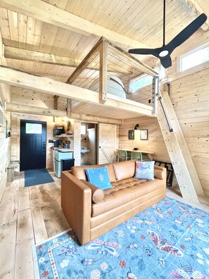 Un vaste espace de vie de style loft, doté d’un plafond haut, d’un ventilateur de plafond, d’un canapé agrémenté de coussins décoratifs, d’un coin repas avec une table et des chaises, et d’un coin cuisine avec un évier et un plan de travail.