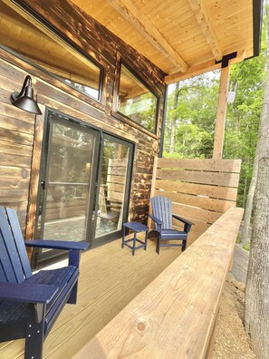 Une terrasse en bois avec une porte vitrée, deux fauteuils Adirondack et un banc.