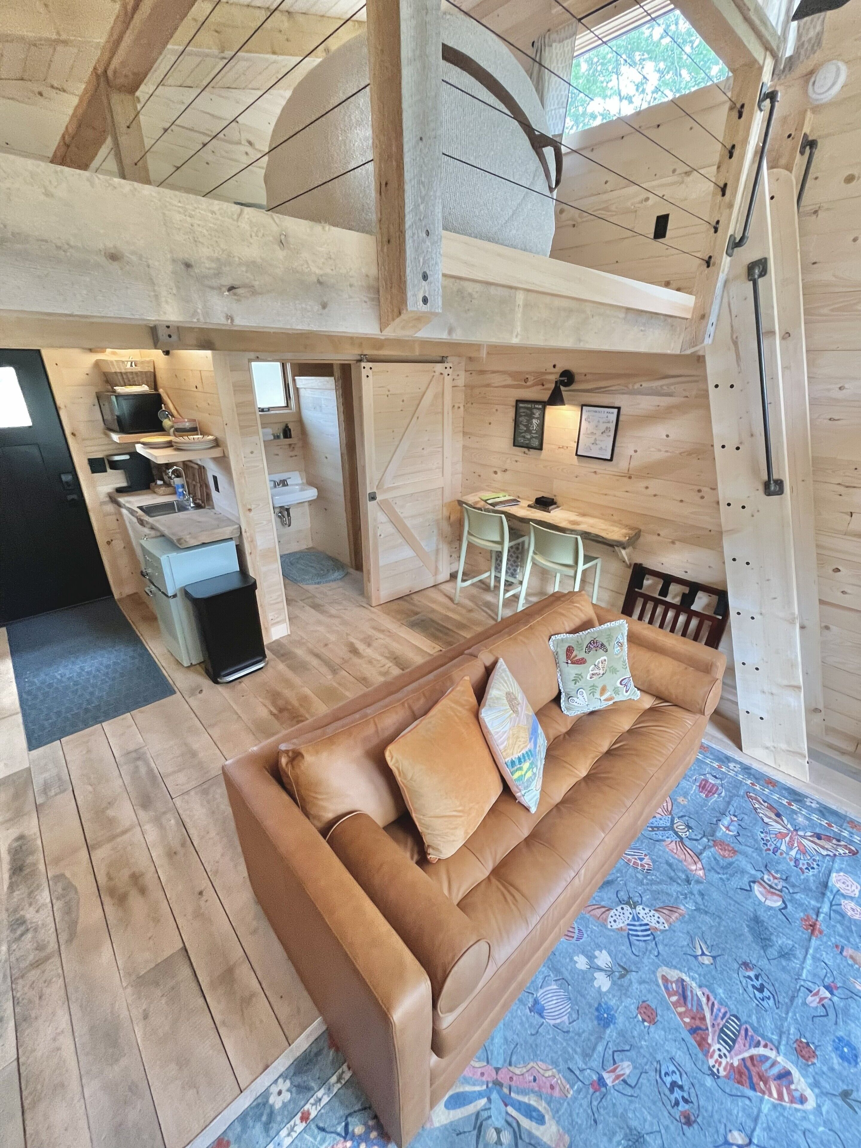 A wooden interior with a brown leather sofa, a dining table with chairs, a kitchen area, and a large wooden door.