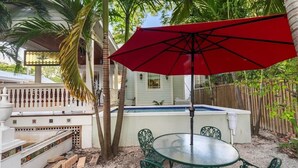 A patio with a glass table and chairs, a red umbrella, and a pool. - "CRAWL" off DUVAL Cottage—only 50 short Steps to the FUN!! (Key West)