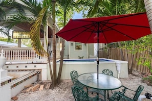 Eine Terrasse mit einem Glastisch und Stühlen, einem roten Sonnenschirm und einem Pool.