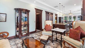 A spacious room with a large wooden cabinet, a dining area with a table and chairs, and a kitchen visible through an open doorway. - "CRAWL" off DUVAL Cottage—only 50 short Steps to the FUN!! (Key West)