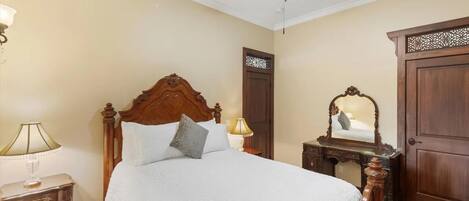 A bedroom with a wooden bed, a ceiling fan, a nightstand with a lamp, and a mirror on a dresser.