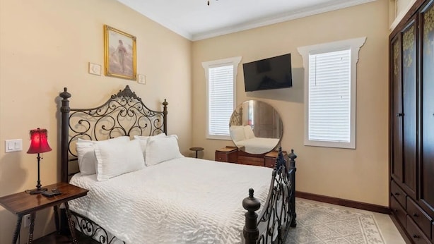 A bedroom with a bed, a bedside table with a lamp, a ceiling fan, a wall-mounted TV, and a window with blinds. - "CRAWL" off DUVAL Cottage—only 50 short Steps to the FUN!! (Key West)