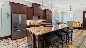 A kitchen with dark wood cabinets, a stainless steel refrigerator, a marble island with bar stools, and pendant lighting. - "CRAWL" off DUVAL Cottage—only 50 short Steps to the FUN!! (Key West)