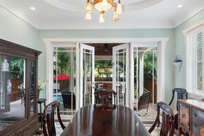A dining area with a large table and chairs, a chandelier, and a view through glass doors to an outdoor patio. - "CRAWL" off DUVAL Cottage—only 50 short Steps to the FUN!! (Key West)