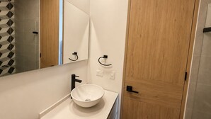 Moderni kylpyhuone, jossa on valkoinen pesuallas, peili ja puinen ovi.
