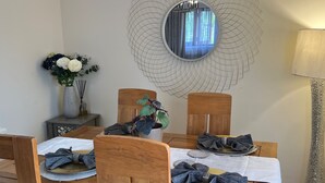 Una mesa de comedor con sillas, un espejo decorativo y un jarrón con flores.